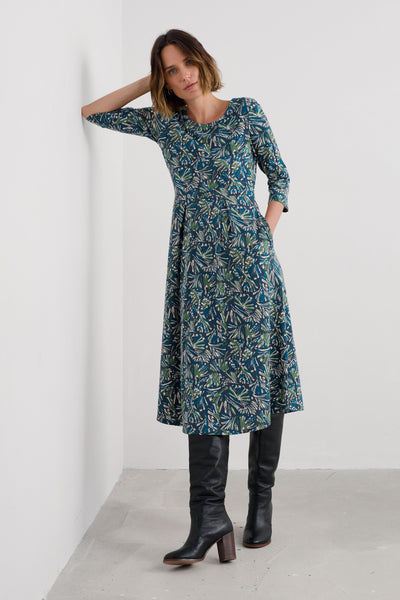 Woman wearing a blue patterned dress and black boots against a white background