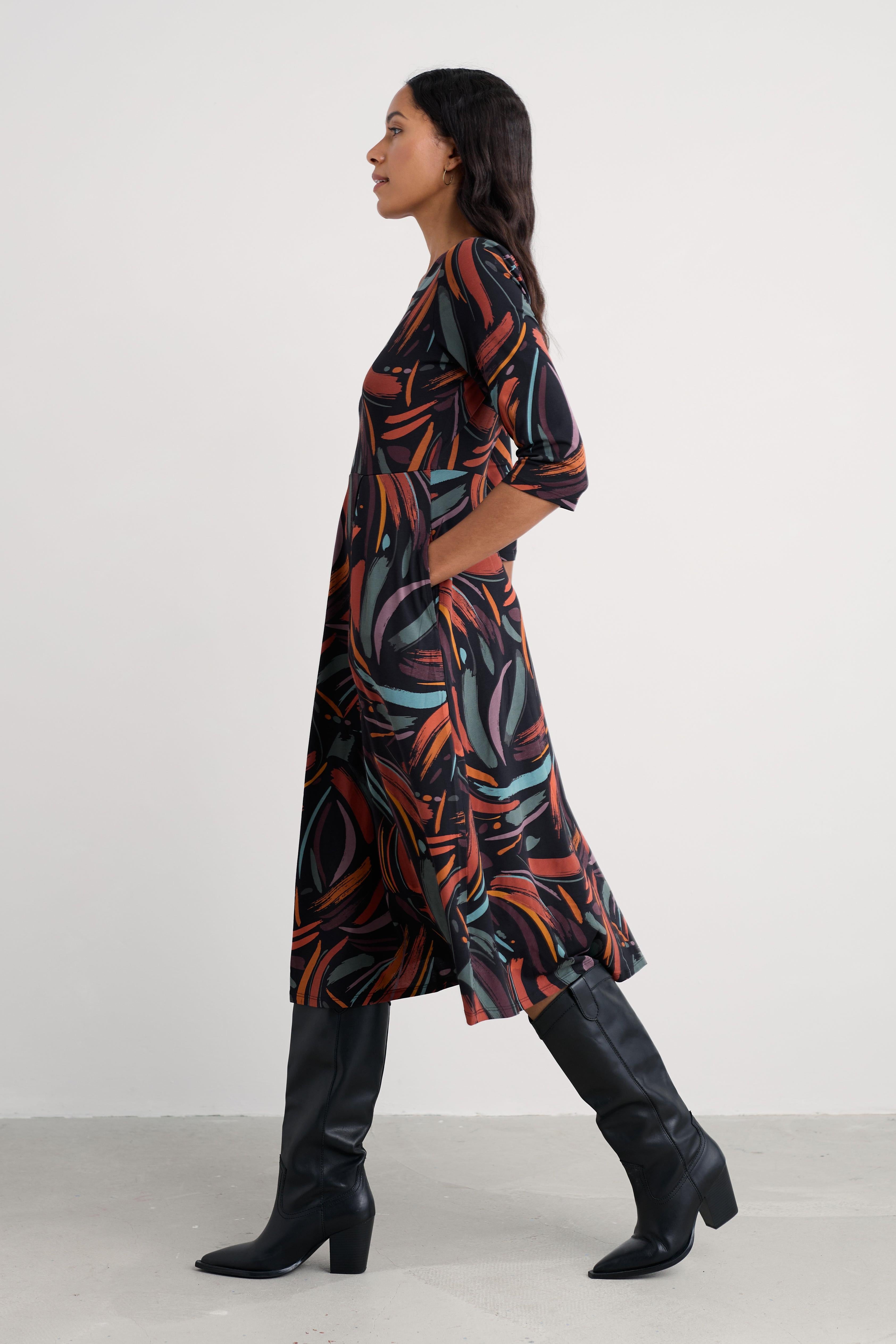 Woman wearing a patterned organic cotton dress and black knee-high boots against a white background