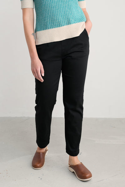 Person wearing black organic cotton trousers and a teal and beige top on a white background