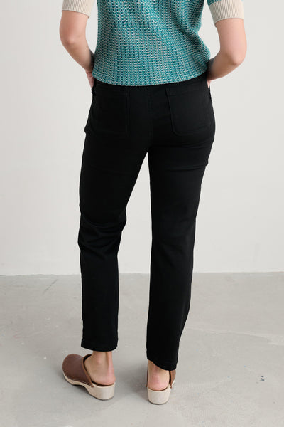 Person wearing a teal knitted top and black tapered trousers on a plain background