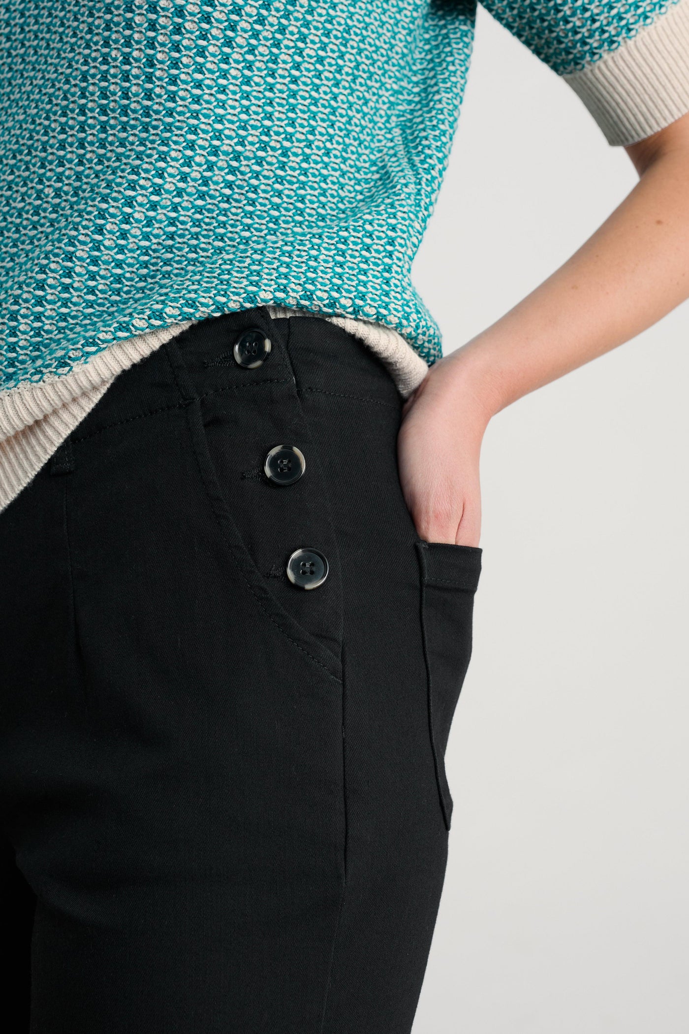 Person wearing a teal knitted sweater with black organic cotton trousers on a light gray background