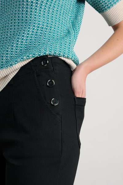 Person wearing a teal knitted sweater with black organic cotton trousers on a light gray background