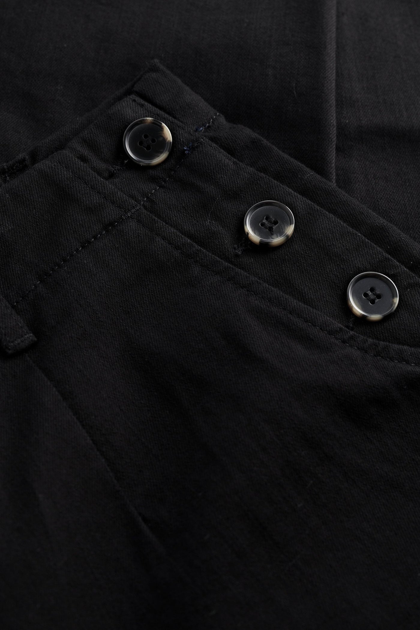 Close-up of a black tapered trousers with buttons on the pocket