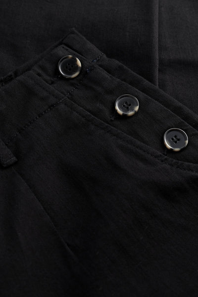 Close-up of a black tapered trousers with buttons on the pocket