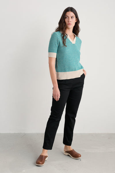 Woman wearing a teal knitted sweater and black organic cotton pants on a white background