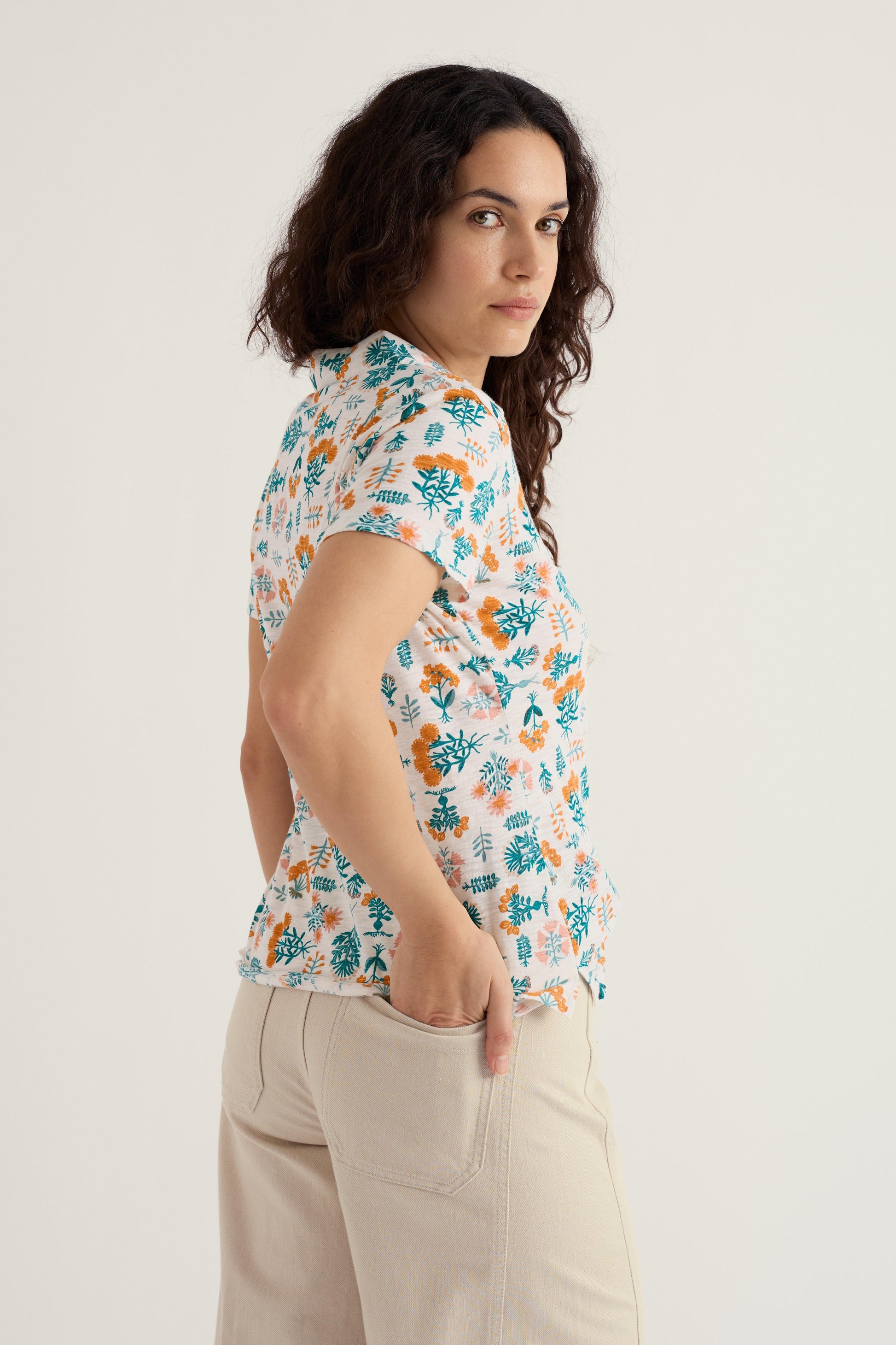 Woman wearing a floral short-sleeve shirt and beige barrel jeans on a light background