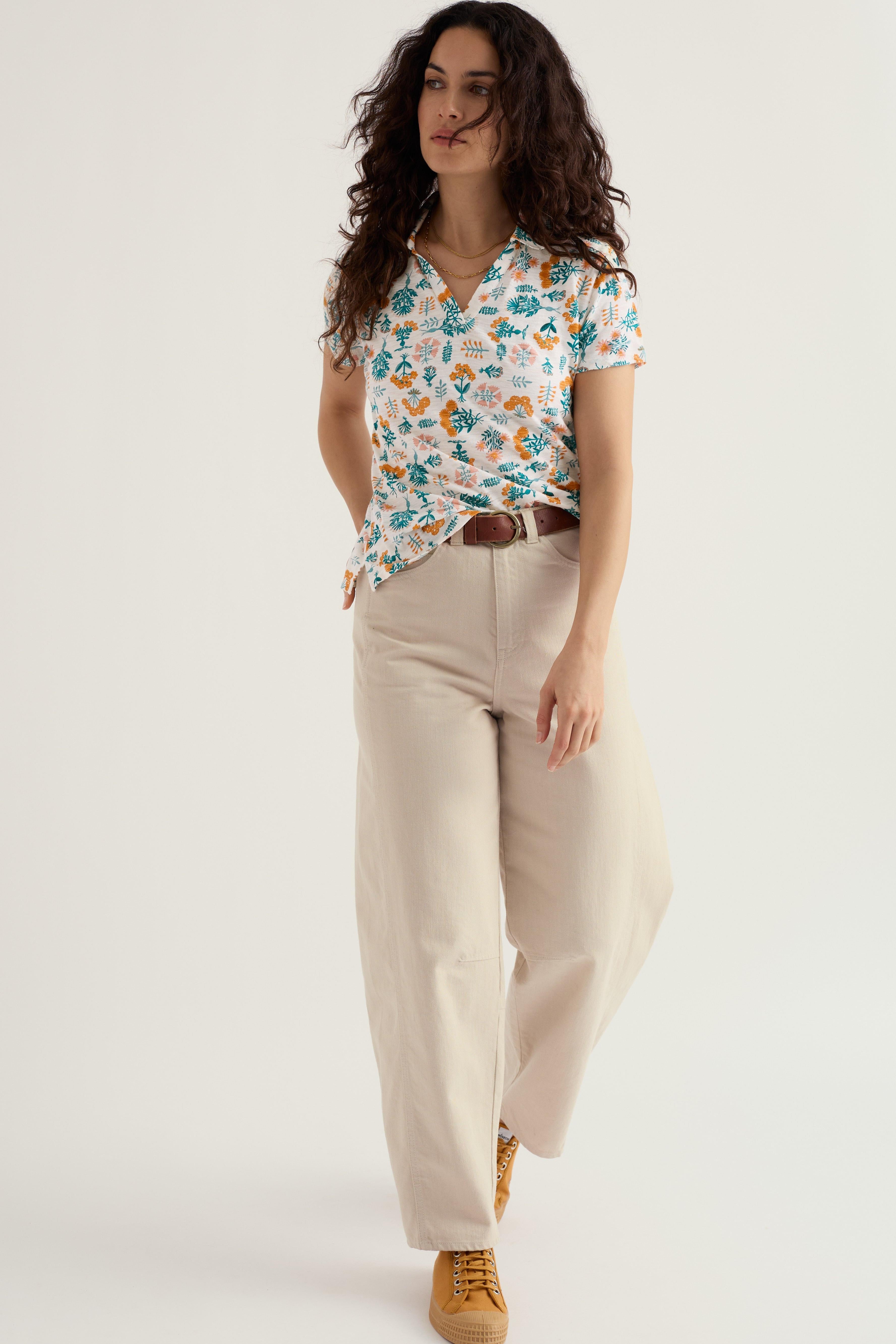 Woman wearing a floral organic cotton blouse and barrel leg jeans on a white background