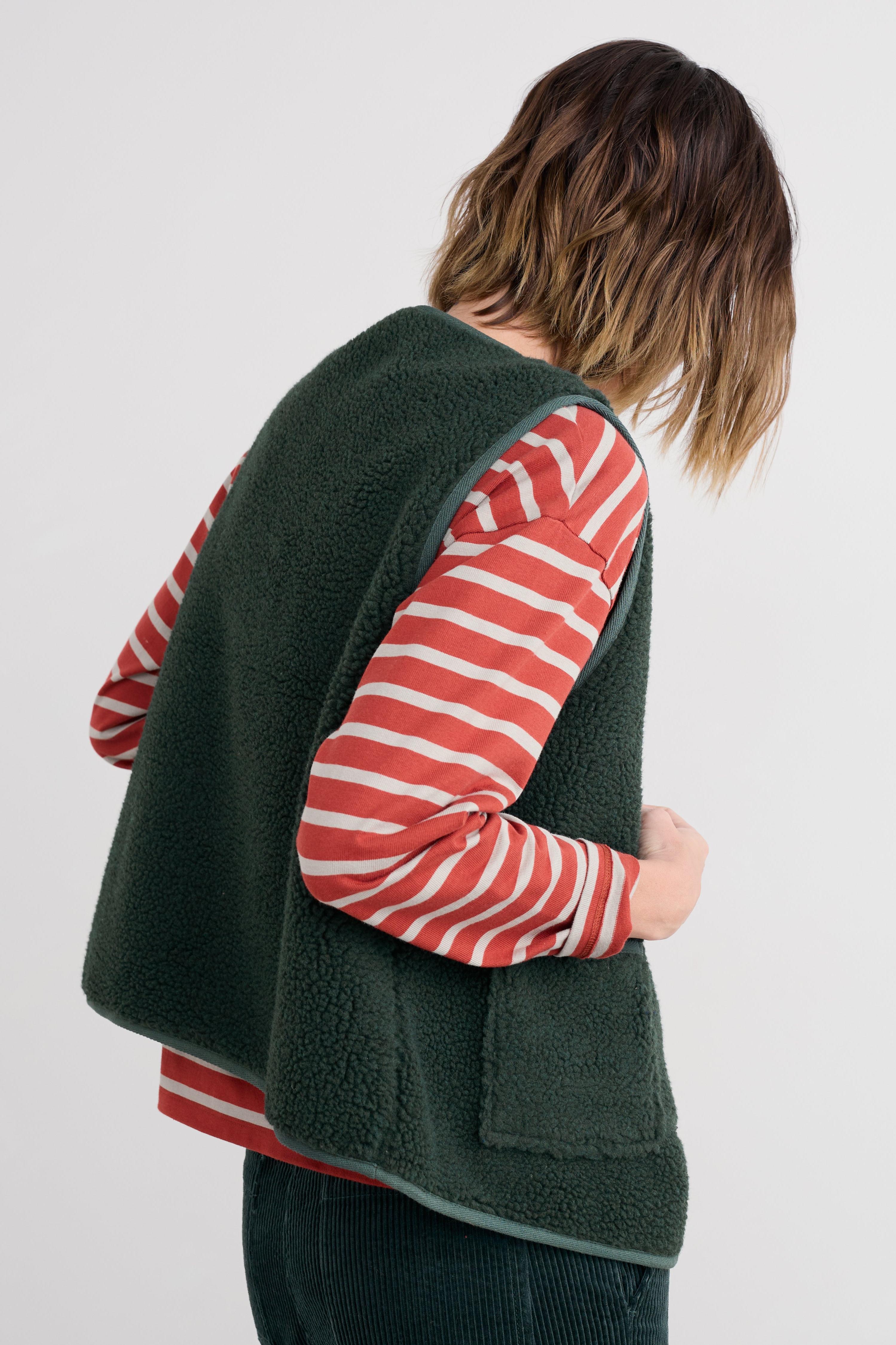Person wearing a green fleece vest over a red and white striped shirt on a plain background