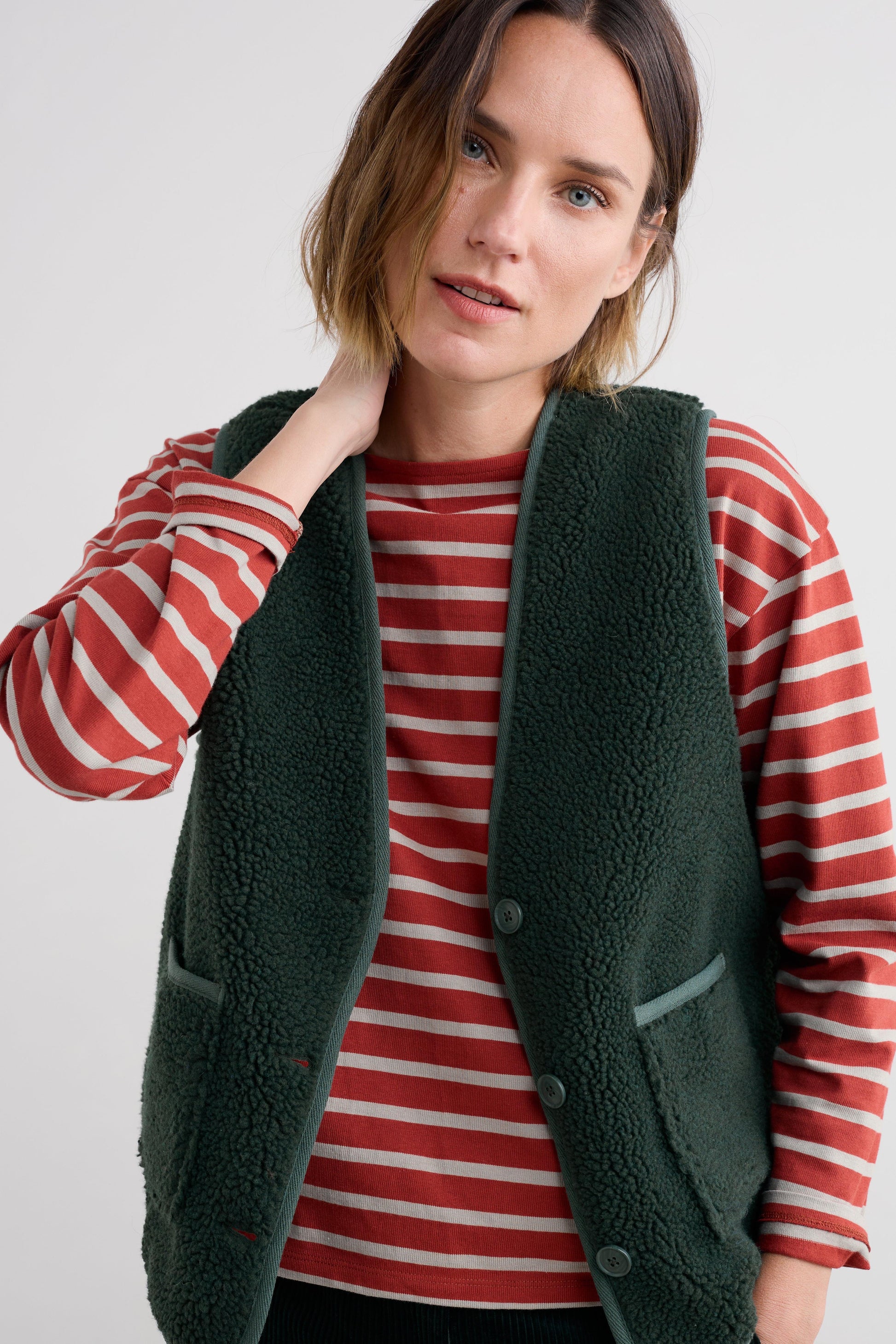 Woman wearing a green fleece gilet over a red and white striped shirt on a plain background