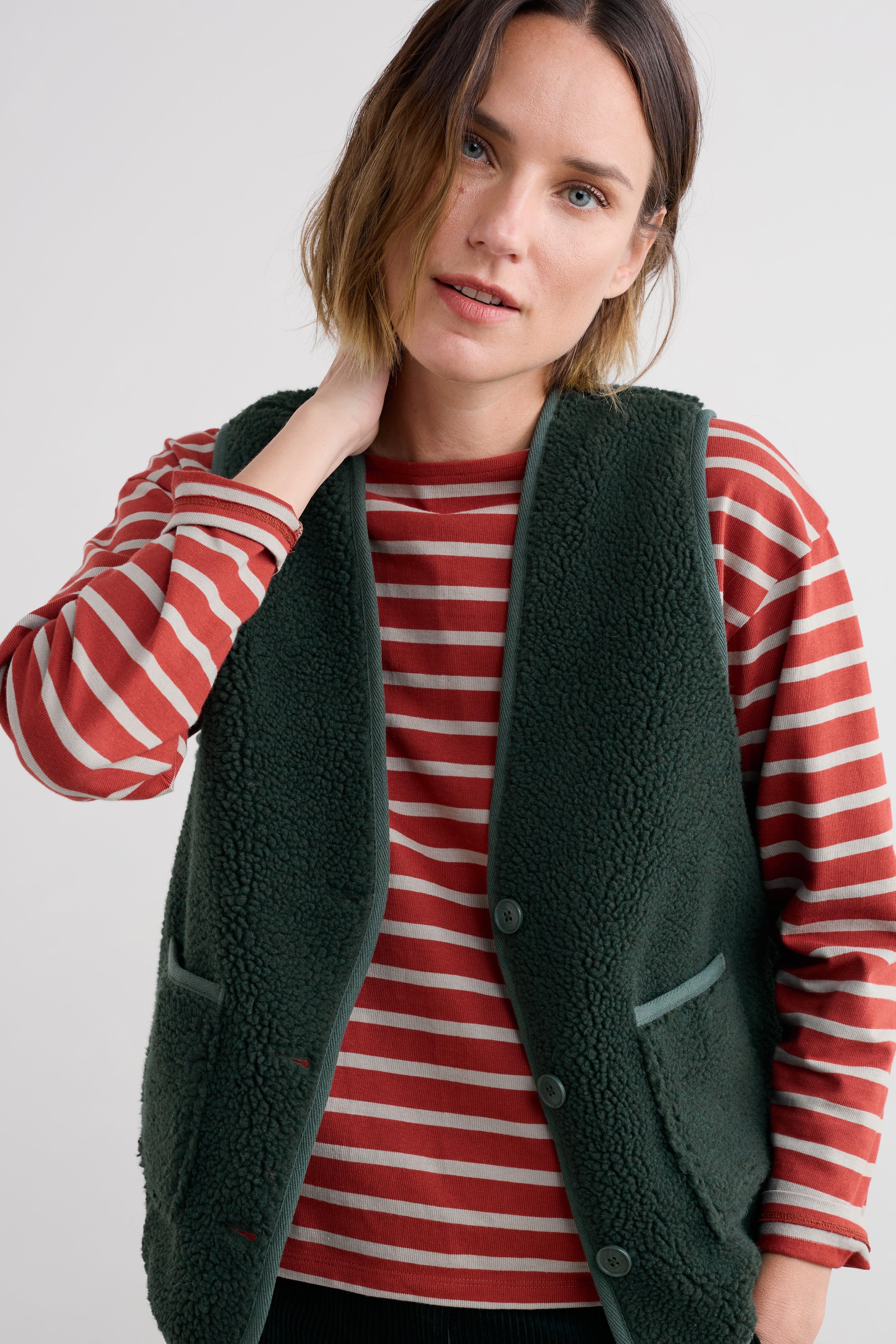 Woman wearing a green fleece gilet over a red and white striped shirt on a plain background