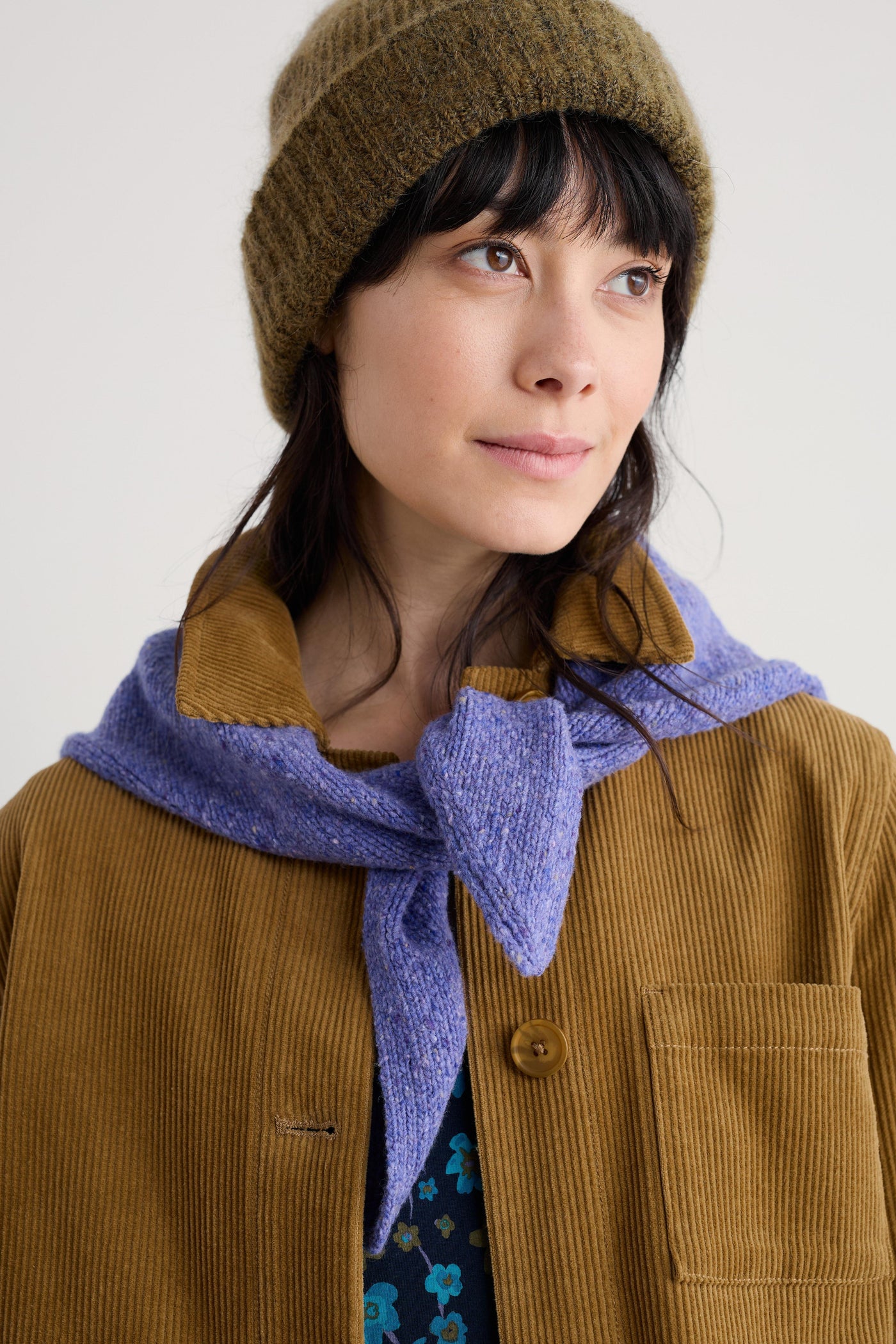 Person wearing a brown beanie and coat with a purple merino wool scarf on a white background