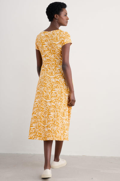 Side view of model wearing the yellow floral dress with white trainers.