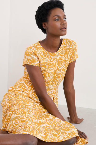 Model seated on the ground wearing the floral Seasalt dress, smiling and relaxed.