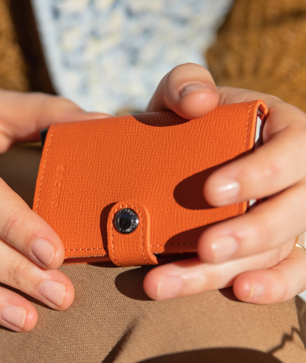 Orange wallet held by hands on a brown surface