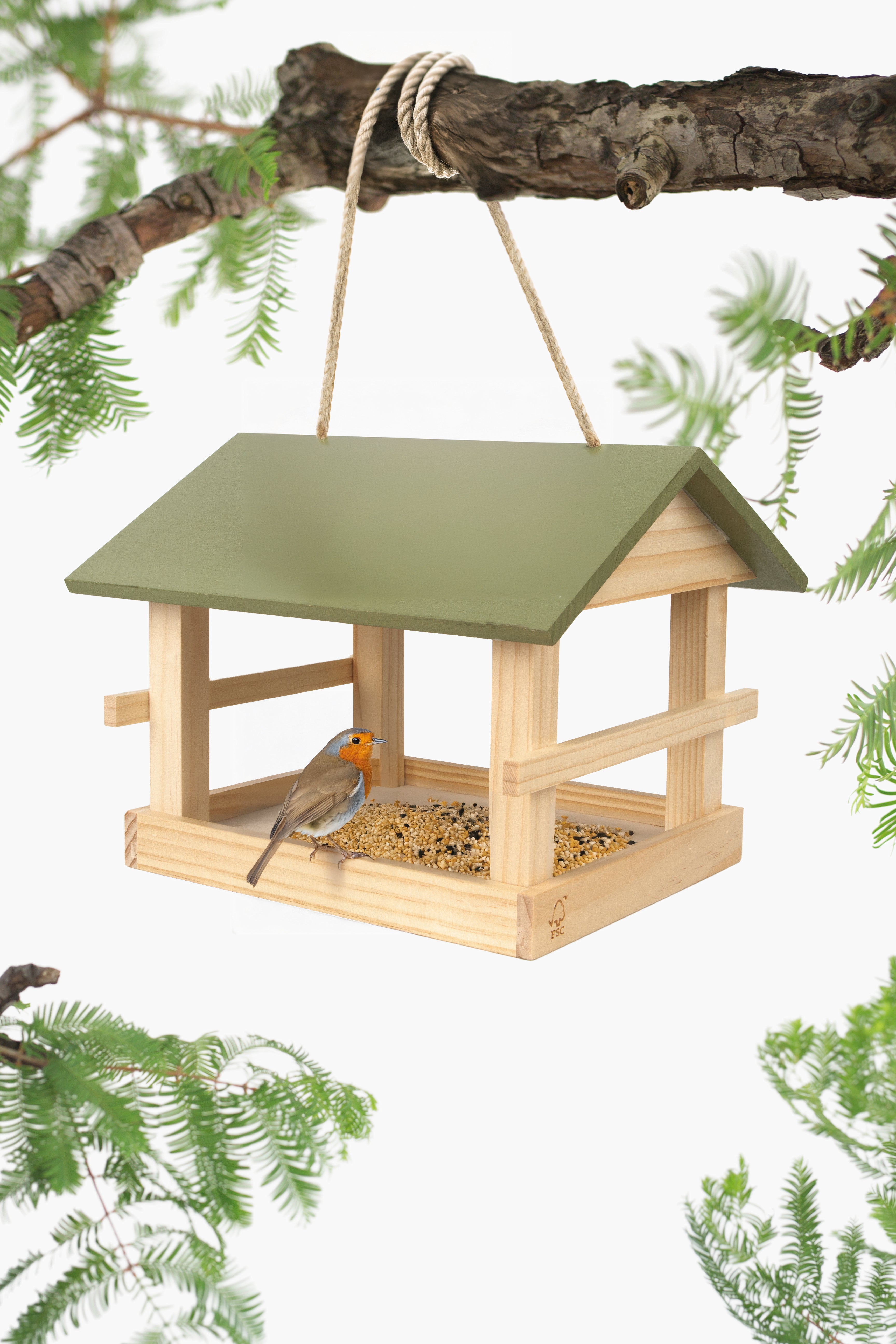 Wooden bird feeder with a green roof, hanging from a branch with green foliage in the background.