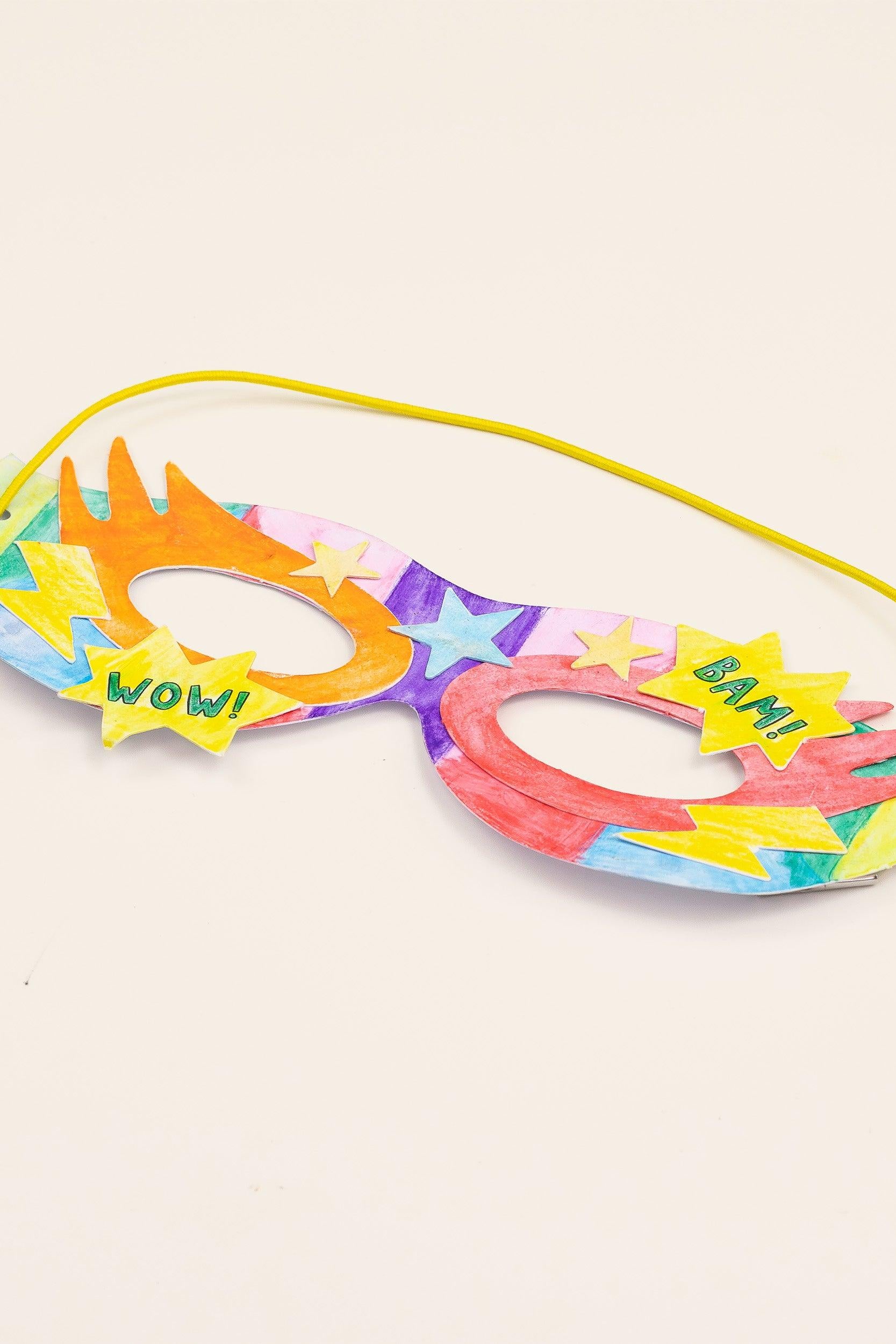 Handmade colorful paper superhero mask with comic book style text.