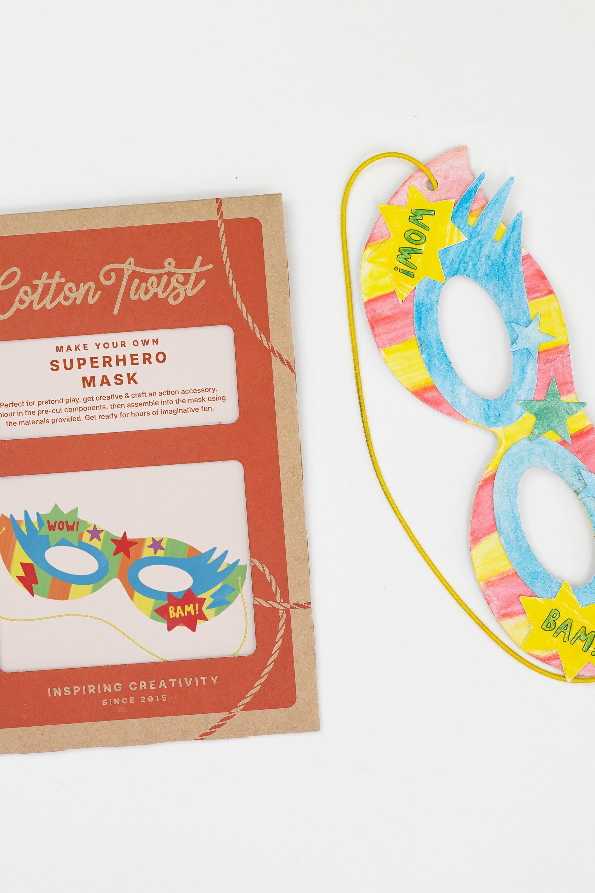A DIY superhero mask craft kit with a colorful hand-decorated cardboard mask and product packaging.