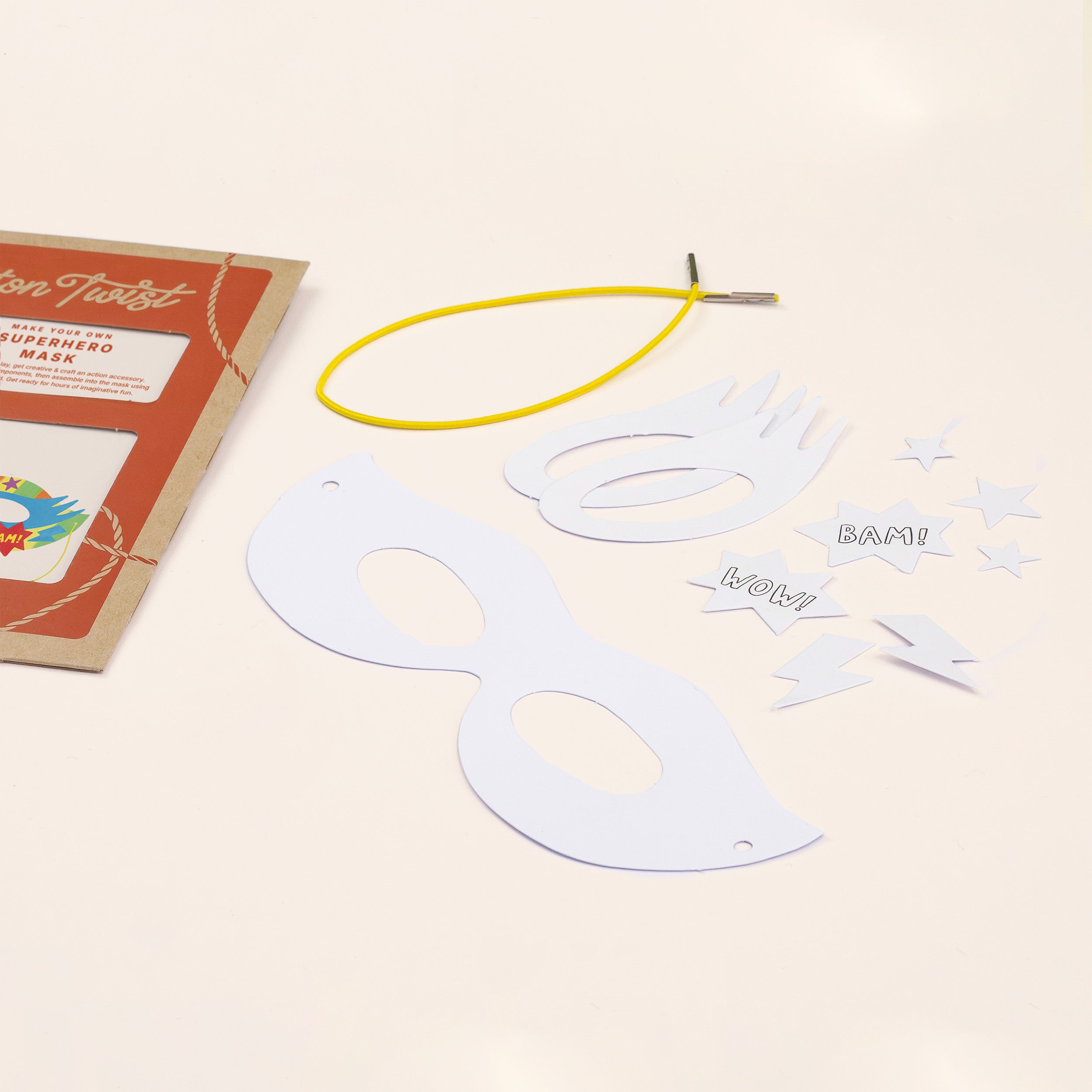 DIY superhero mask craft kit with white paper mask, yellow elastic band, and comic book style cutouts.