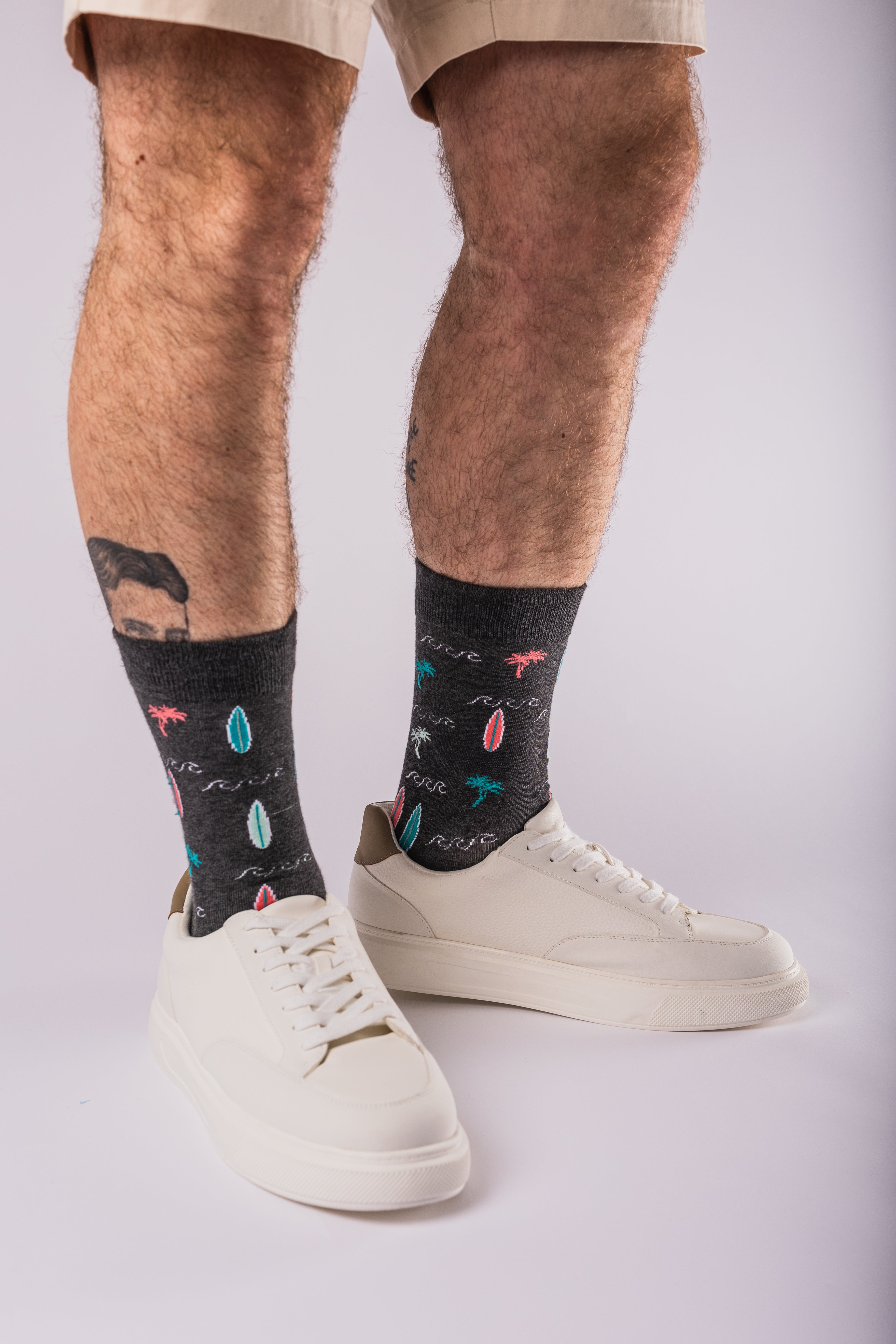 Person wearing black bamboo socks with colorful designs and white sneakers on a light gray background