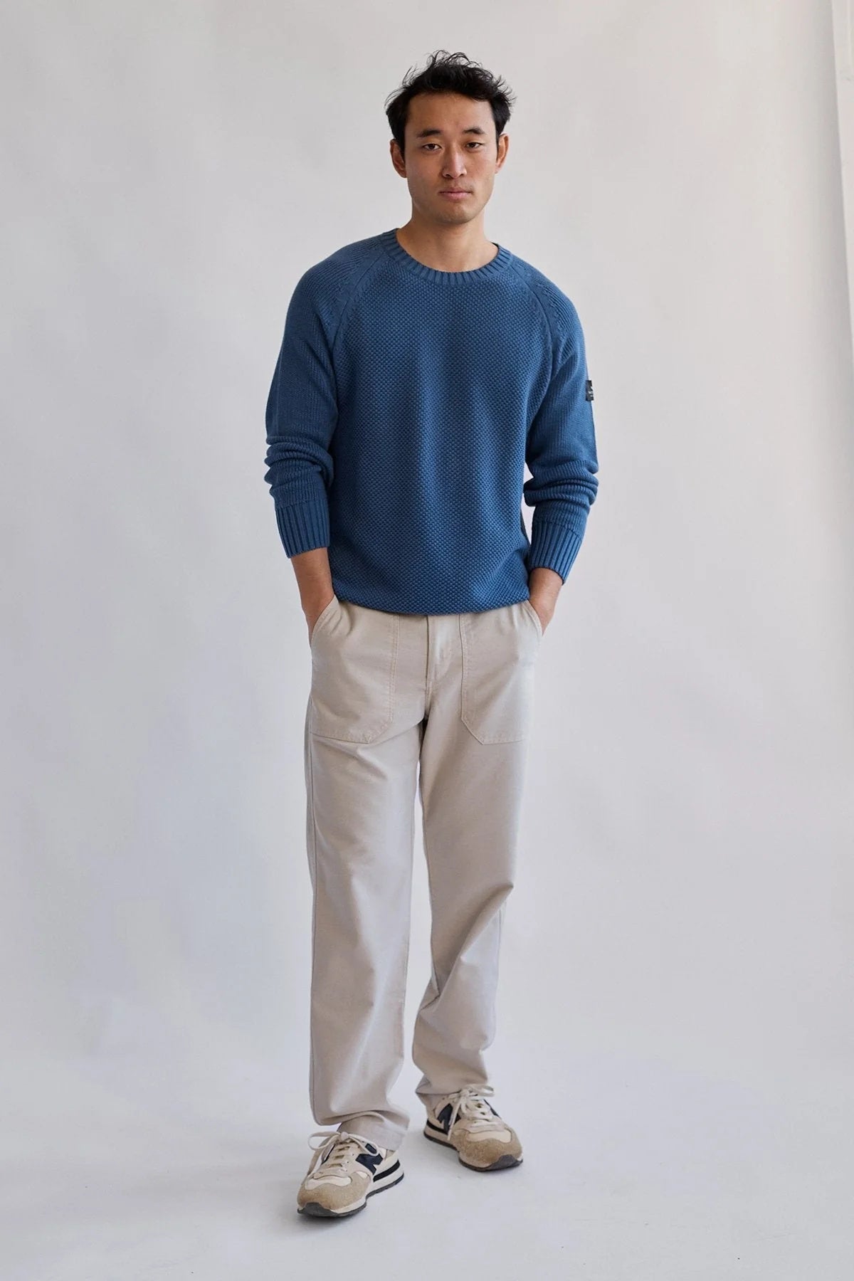 Model wearing the TWOTHIRDS Tortuga sweater in blue paired with ecru casual trousers and new balance trainers.