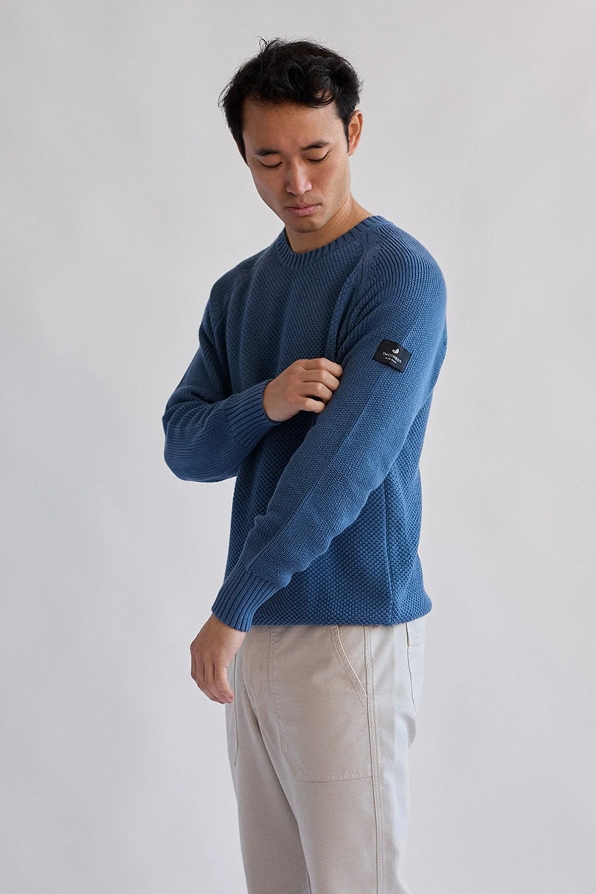 Front view of model wearing the TWOTHIRDS Tortuga sweater in blue, highlighting TWOTHIRDS logo on arm and ribbed edges.