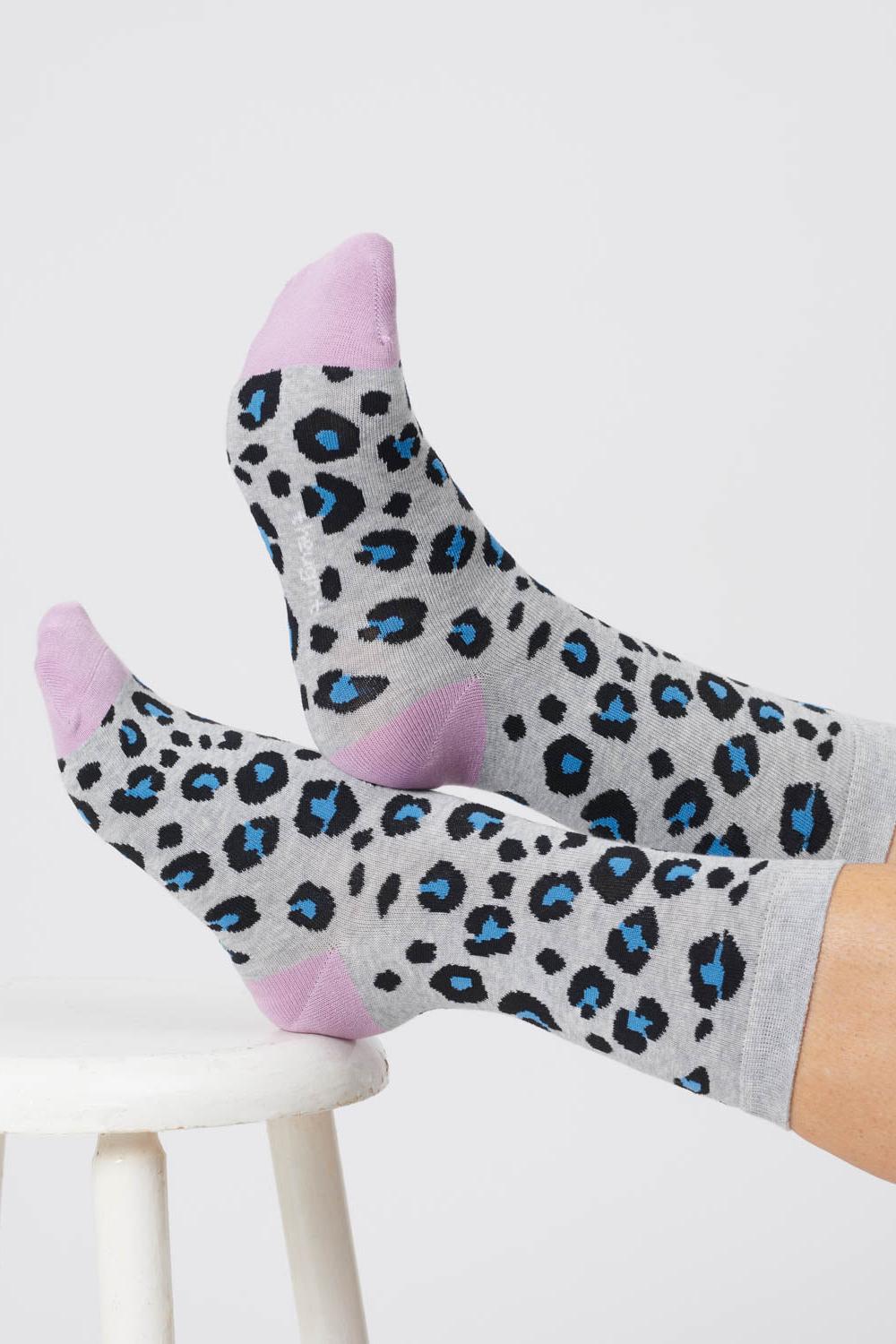 Feet crossed on stool wearing grey bamboo socks with blue animal print spots and lilac heels and toes.