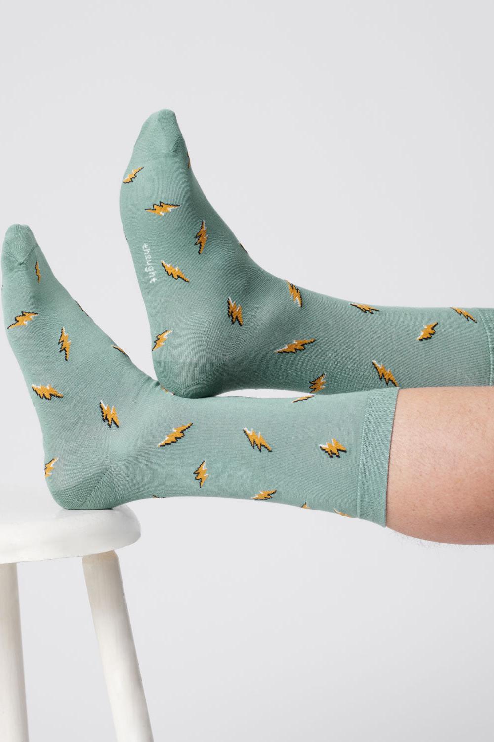 Close-up of feet wearing lagoon green socks with lightning bolt patterns, crossed and resting on a stool.