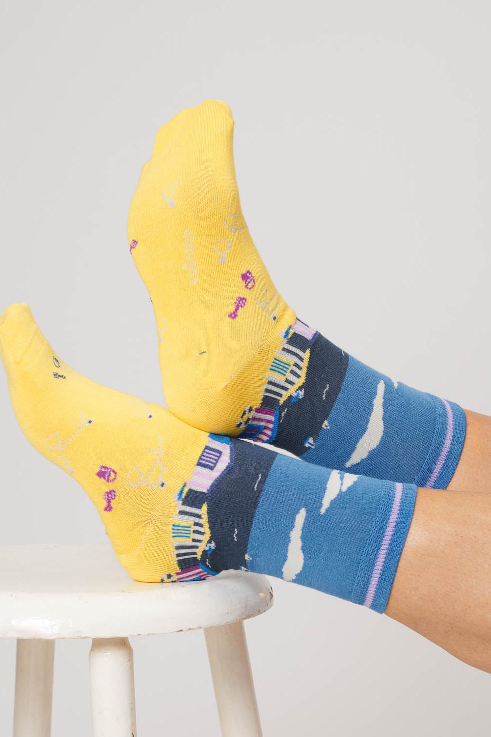 Close-up of feet wearing sea blue socks with a beach hut design, crossed and resting on a stool.