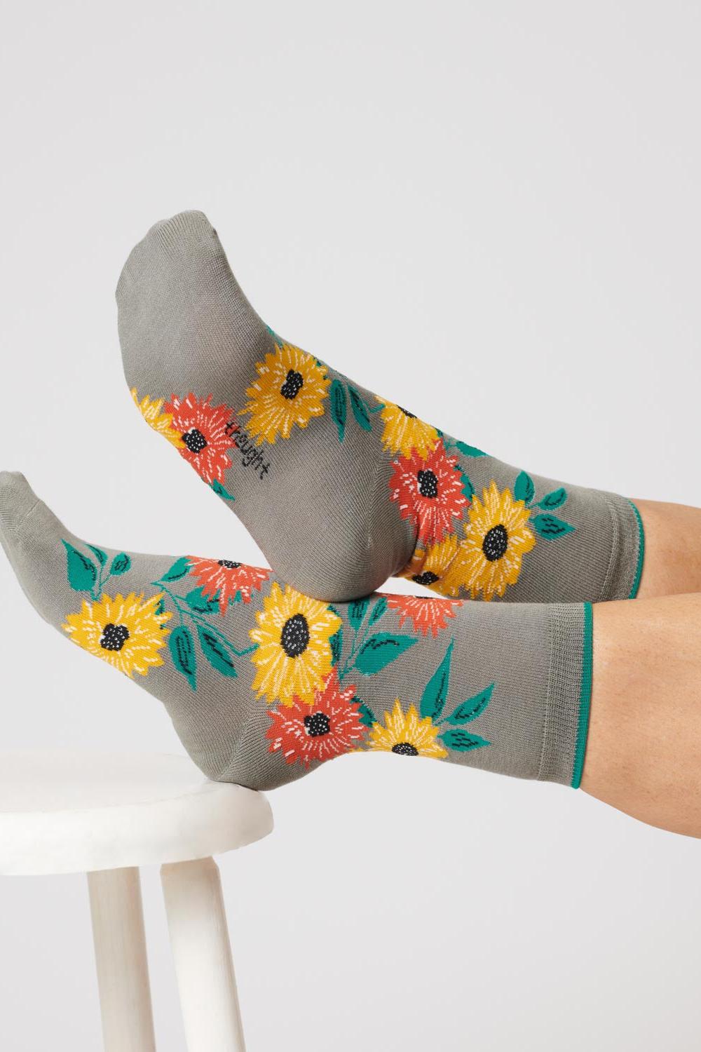 Close-up of feet wearing olive green socks with a sunflower design, crossed and resting on a stool.