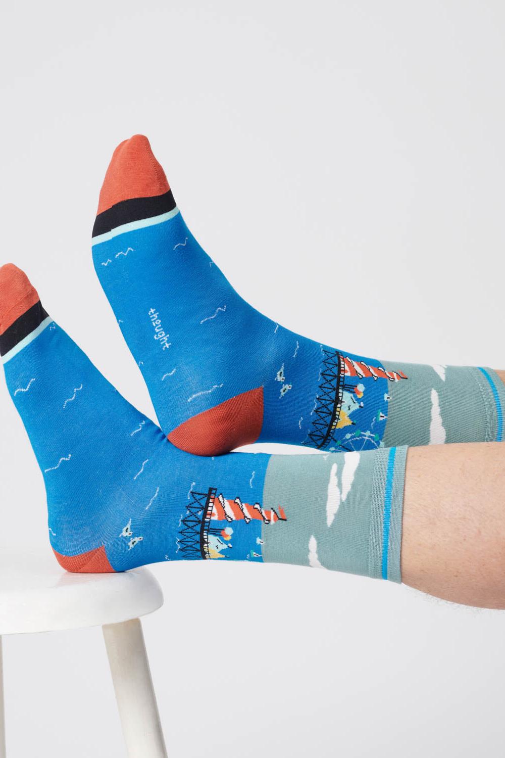 Close-up of feet wearing lagoon green socks with a waterfront scene design, crossed and resting on a stool.