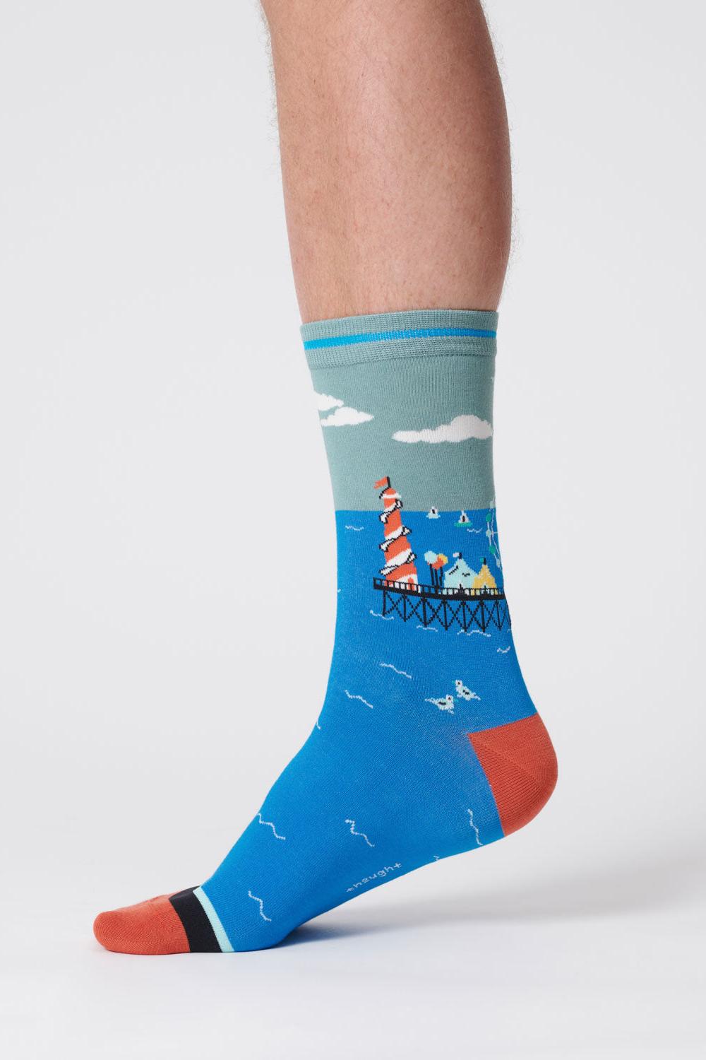 Close-up of a foot wearing a lagoon green sock with a waterfront scene design.