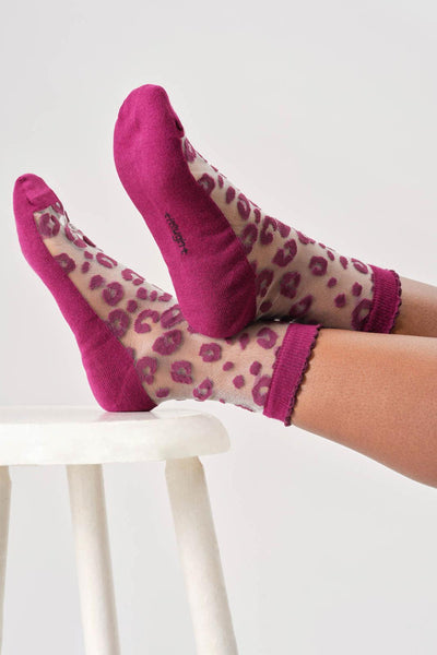 Purple leopard print bamboo socks worn by a person on a white stool against a white background