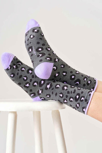 Gray organic cotton socks with black leopard print and purple accents on a white stool.