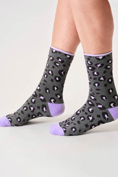 Gray socks with purple accents and a leopard print pattern worn by a person on a light gray background