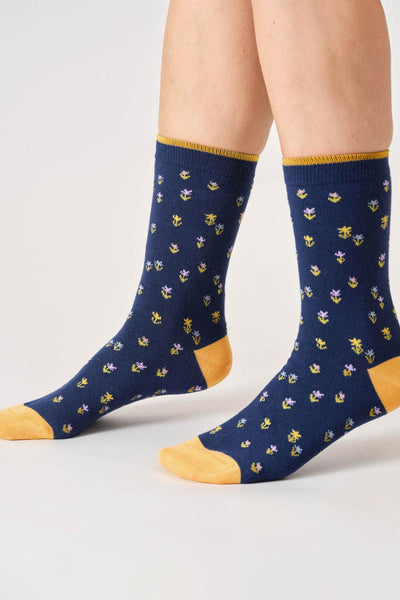 Navy organic cotton socks with floral pattern and yellow accents worn by a person on a light gray background