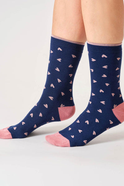Navy socks with pink heart patterns worn by a person on a light gray background