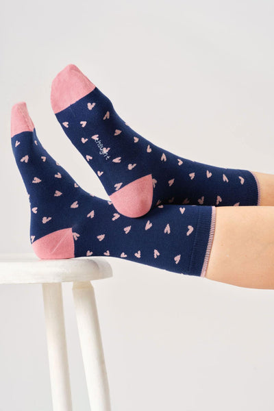 Navy socks with pink hearts worn by a person on a white chair.