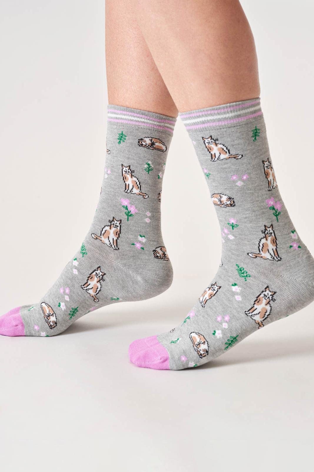 Gray socks with cat patterns worn by a person on a light background