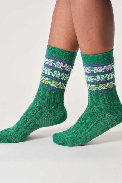 Green knitted wool socks with floral patterns worn by a person on a light gray background