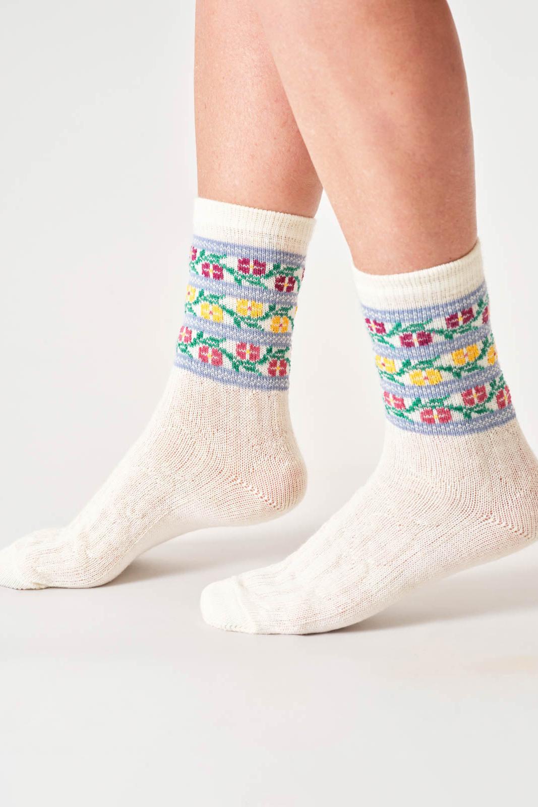 White wool socks with floral patterned cuffs worn by a person on a light gray background