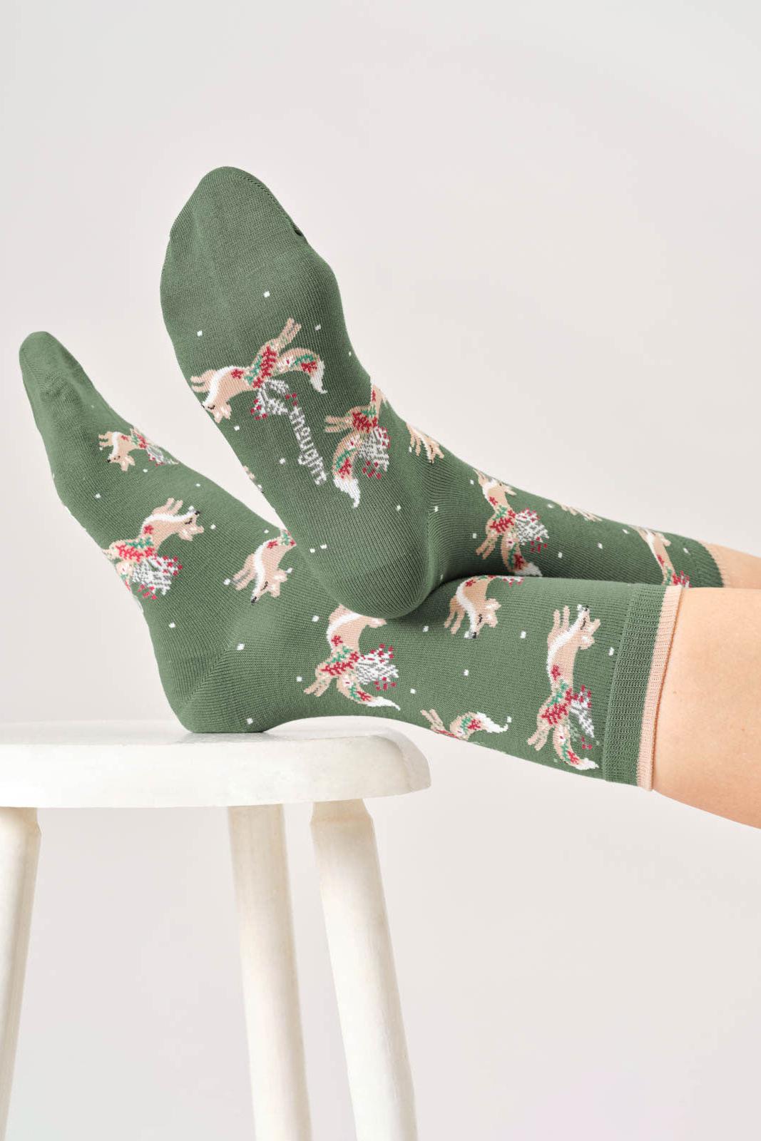 Bamboo green socks with dog and flower pattern worn by a person on a white stool.