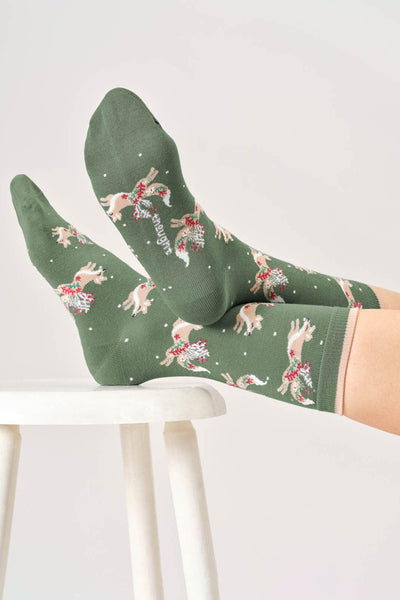 Bamboo green socks with dog and flower pattern worn by a person on a white stool.