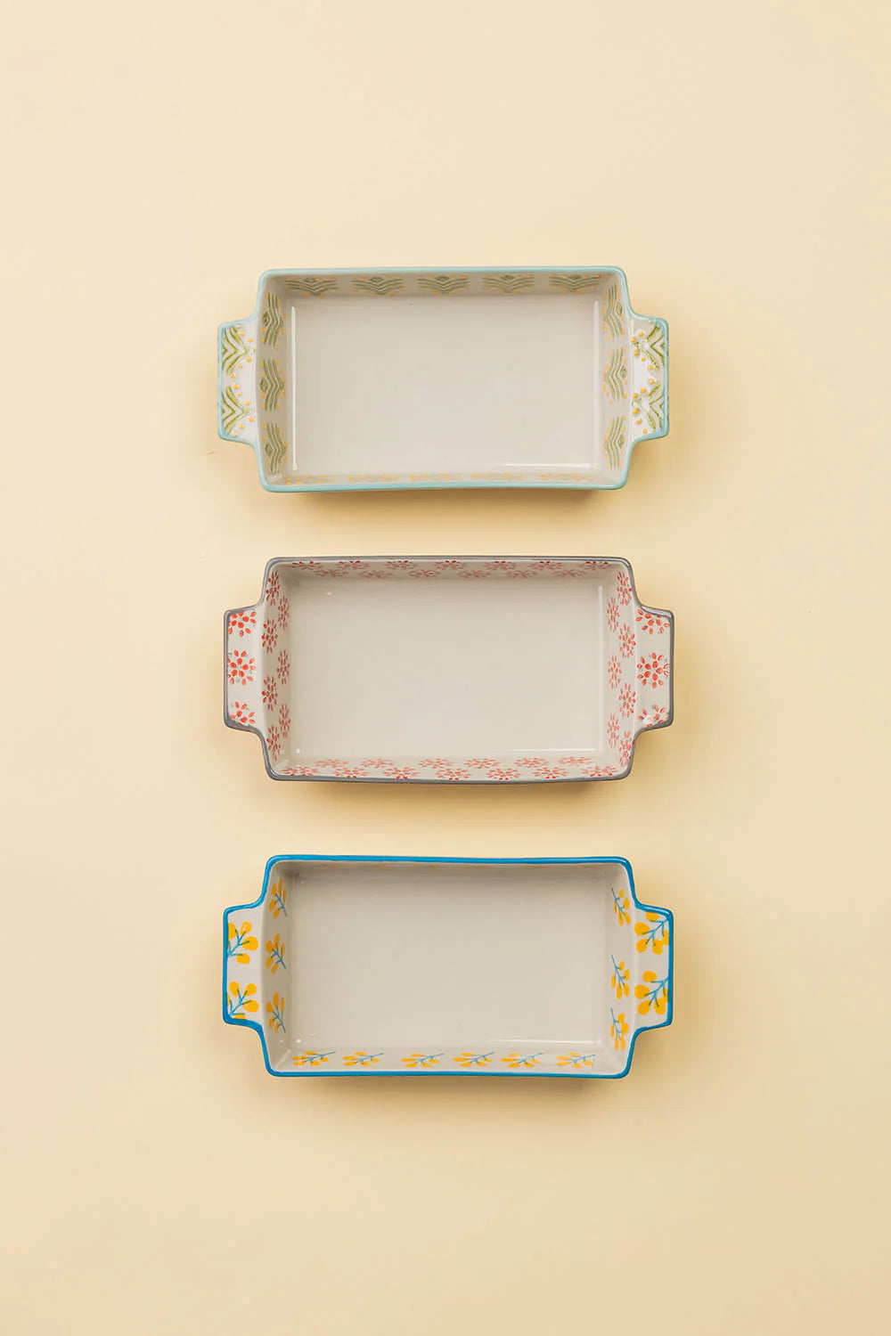 Three rectangular ceramic trays with decorative edges on a beige background