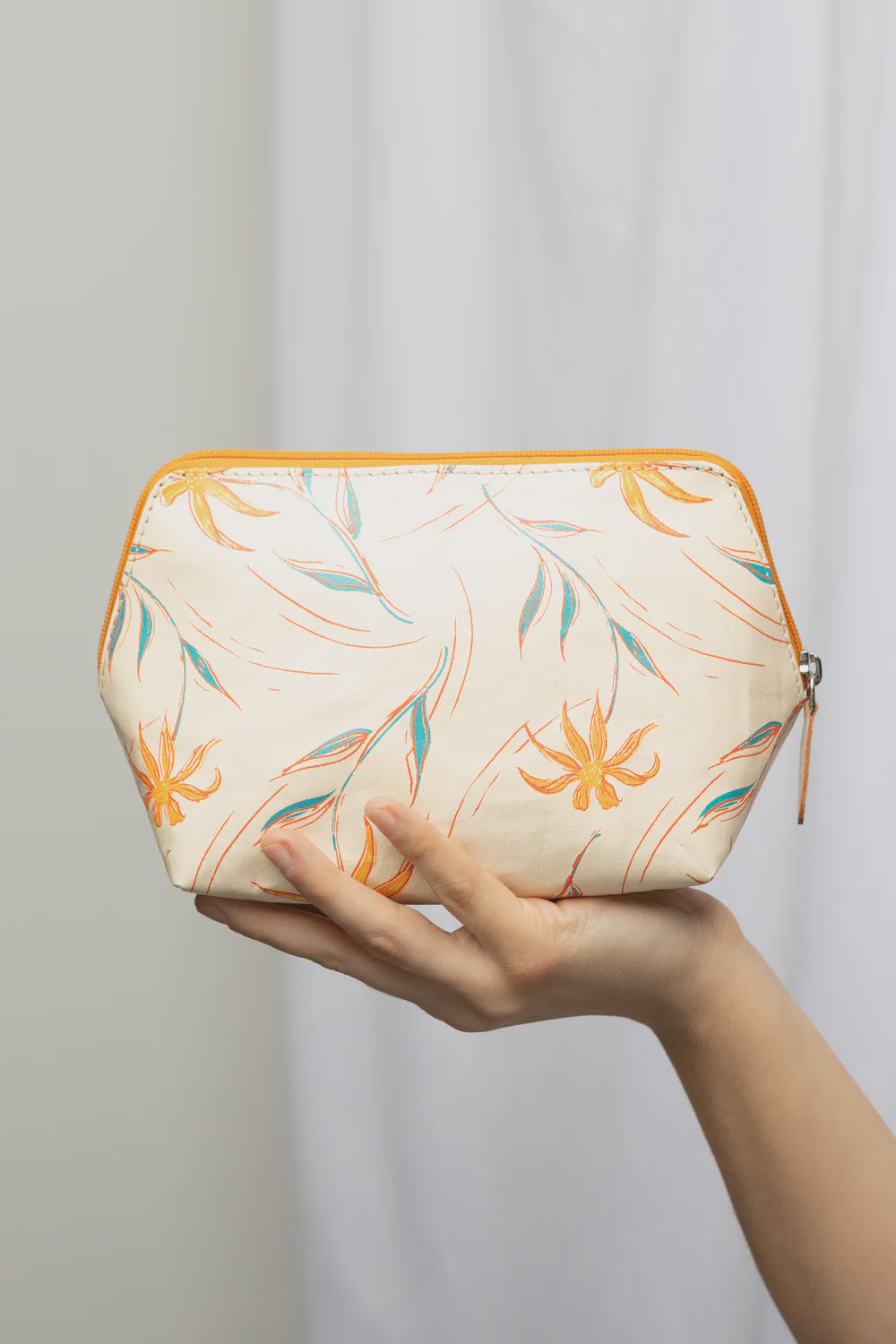 Hand holding a hexagonal pouch with floral pattern against a plain background