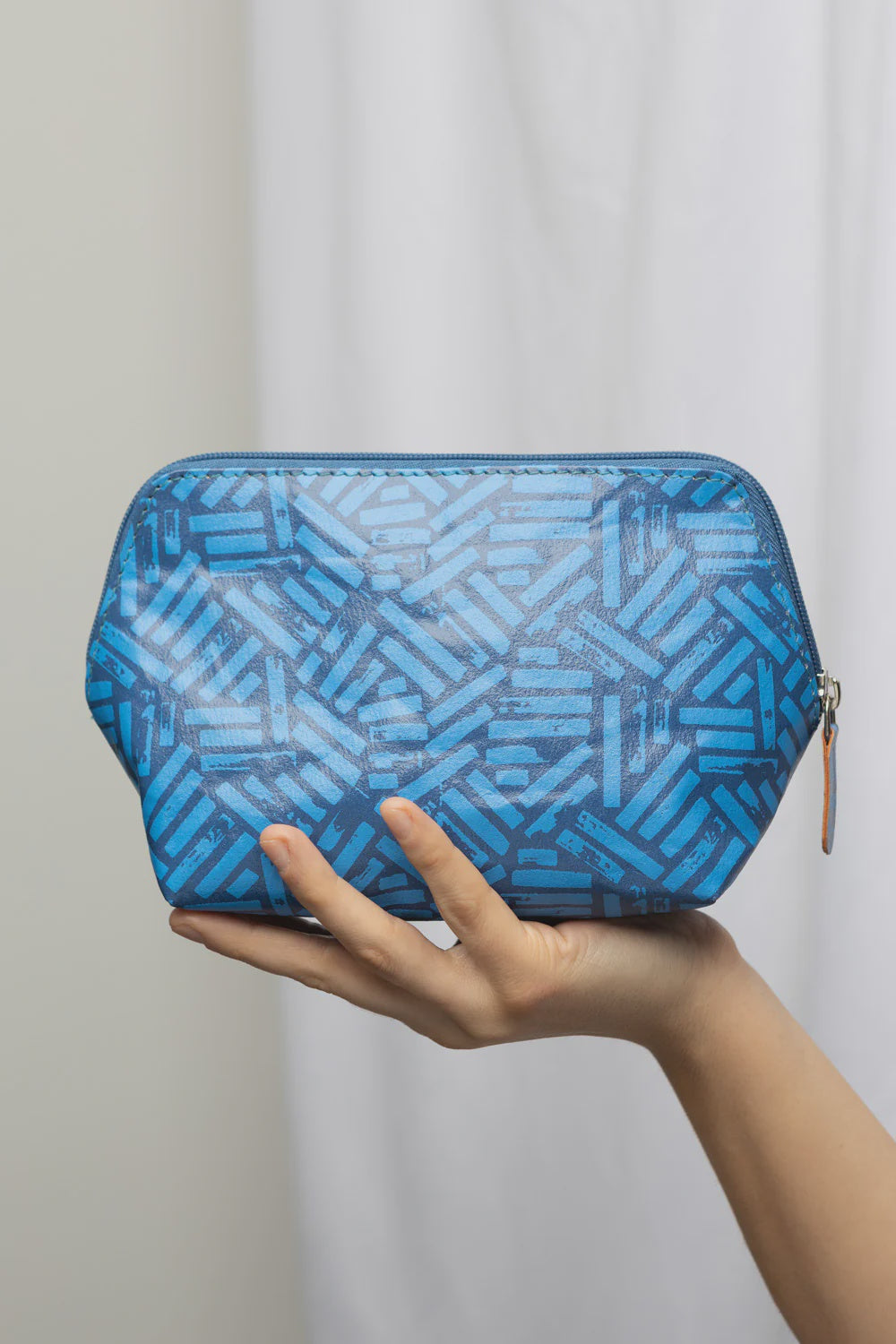 Blue geometric patterned cosmetic bag held in a hand against a plain background