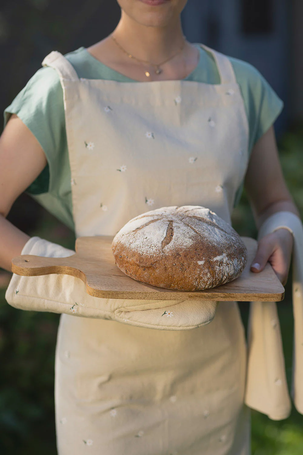 Person wearing an apron holding a wooden cutting board with bread