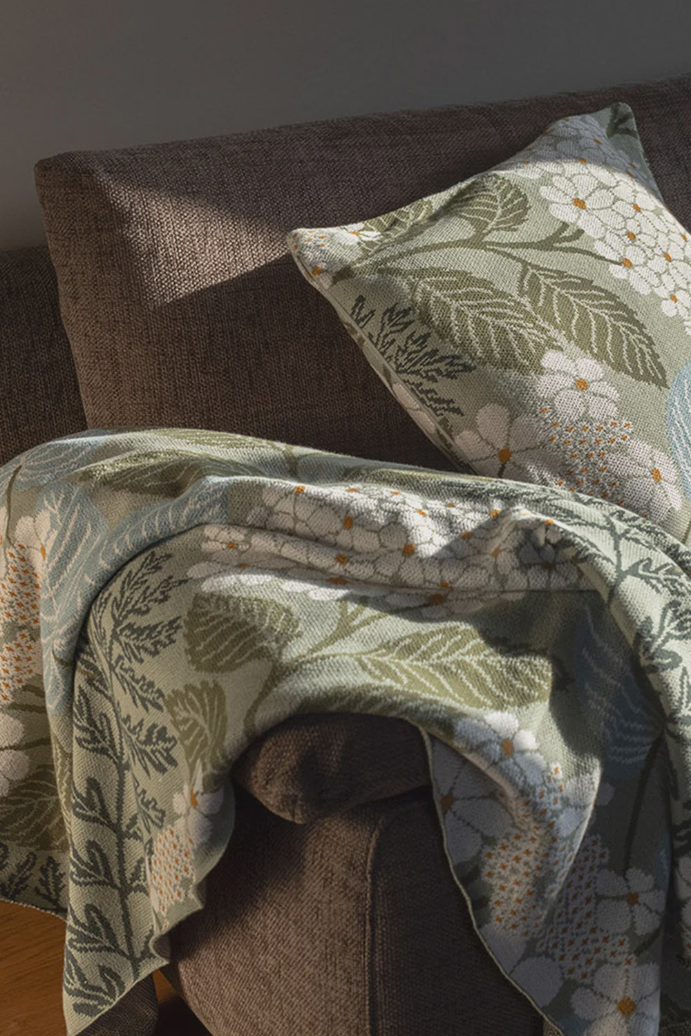 Floral-patterned organic cotton blanket and pillow on a brown sofa