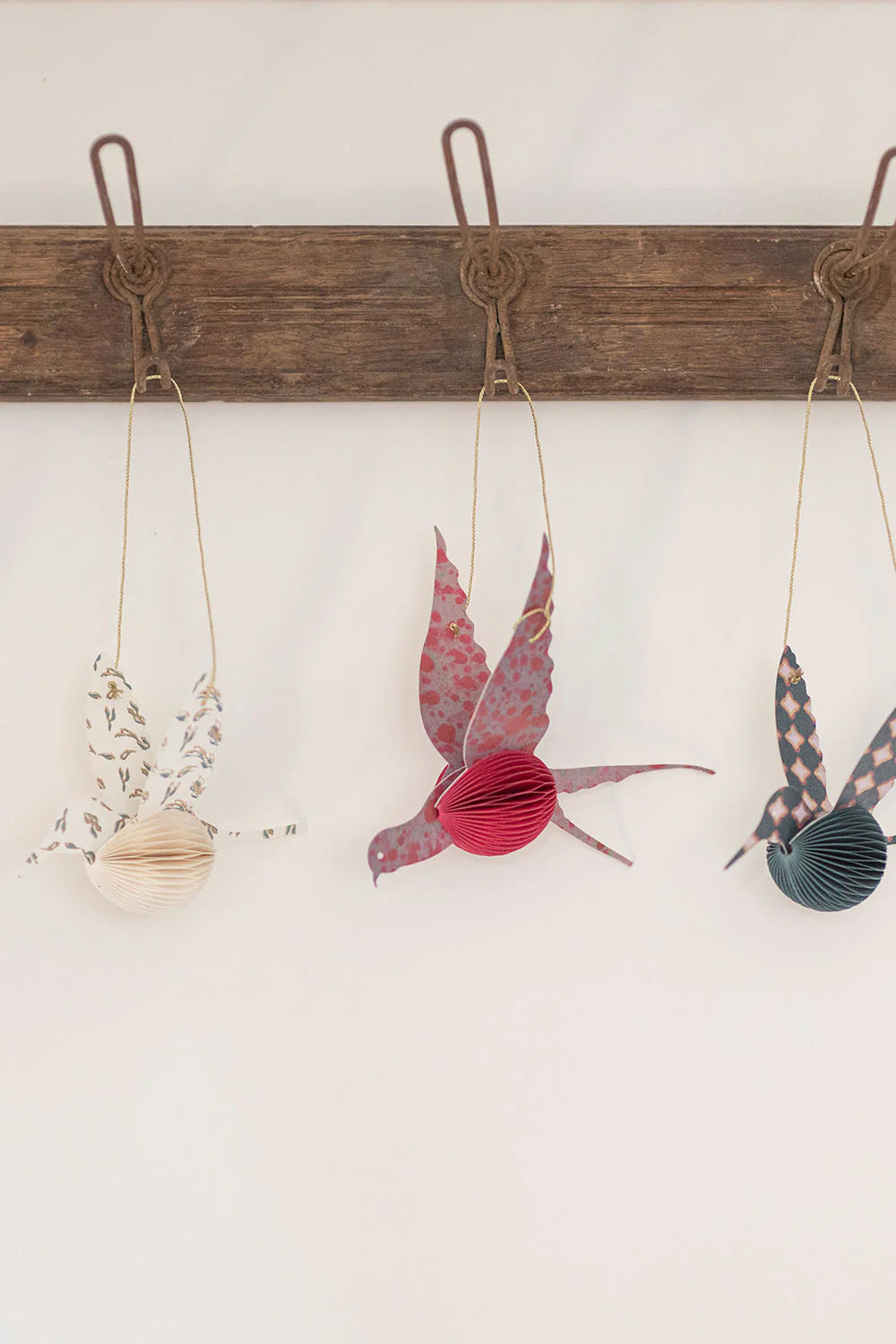 Decorative paper birds hanging on a wooden rod against a white wall.