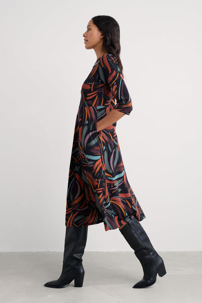 Woman wearing a patterned organic cotton dress and black knee-high boots against a white background
