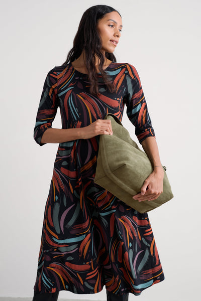 Woman wearing a patterned organic cotton dress holding a green bag against a white background